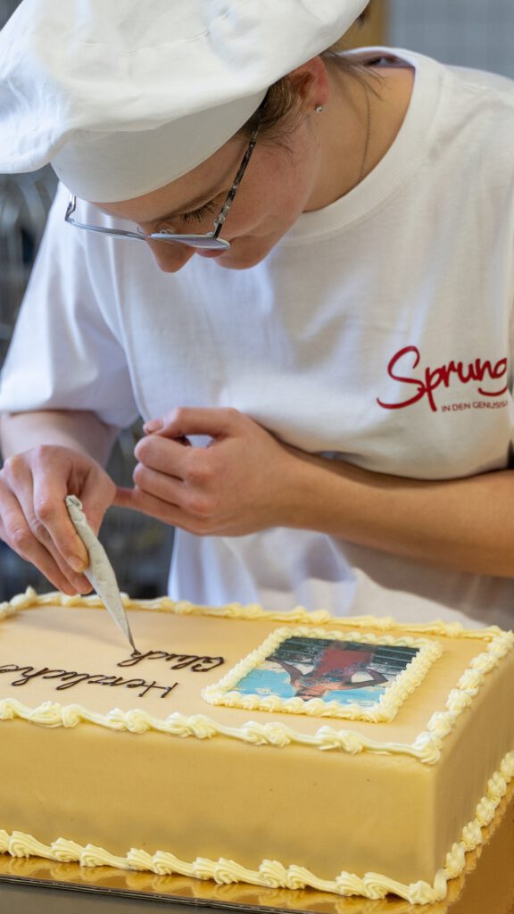 Konditorin verziert einen Kuchen in der Konditorei der Bäckerei Sprung mit einem Schokoladenschriftzug