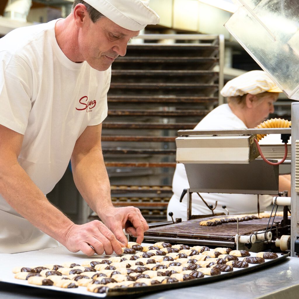 Zwei Mitarbeitende der Bäckerei Sprung formen in der Backstube frisches Süßgebäck
